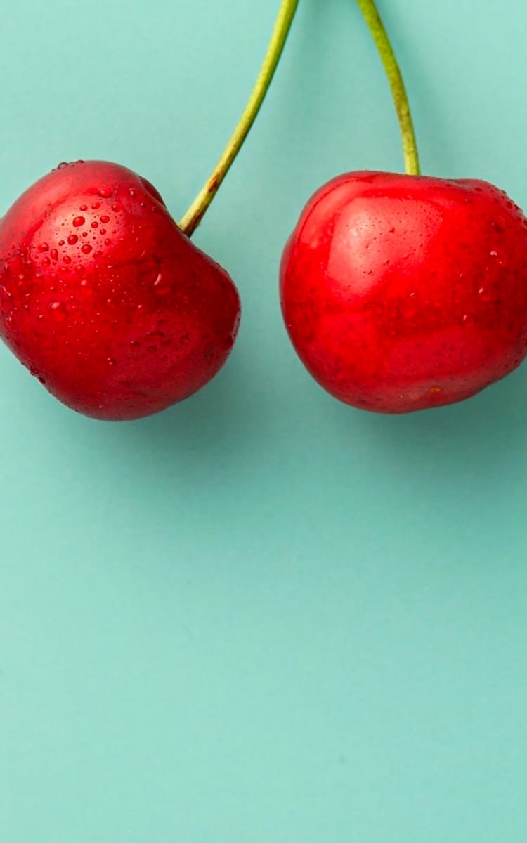 Two red cherries on a green background